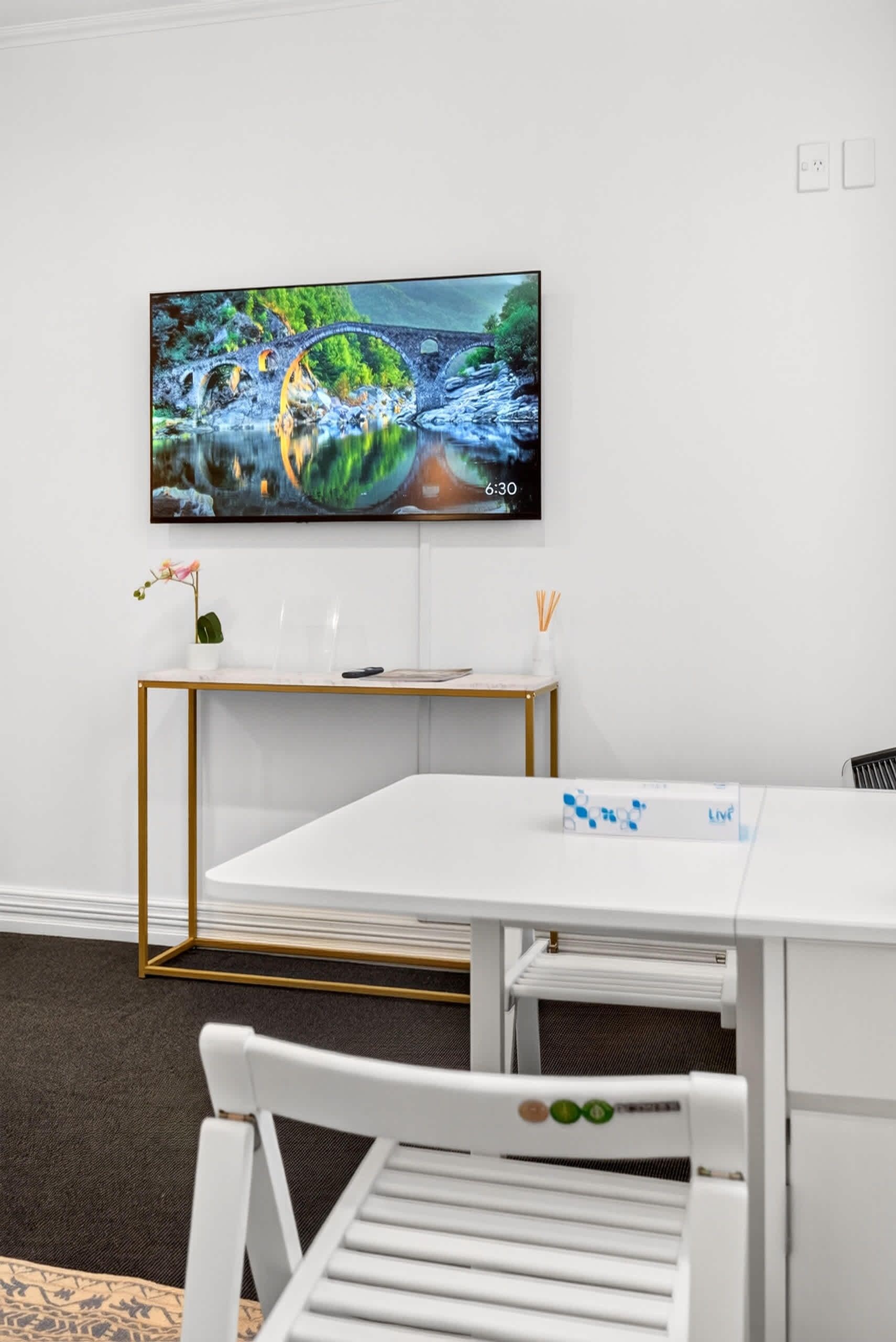 A modern room with a white table, a white chair, a TV mounted on the wall, and a small plant on the table.