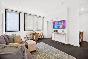 Ein modernes Wohnzimmer mit einer Couch, einem Couchtisch, einem an der Wand befestigten Fernseher und einem Schreibtisch mit Stühlen.
