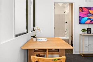 Ein modernes Badezimmer mit Dusche, einem Holztisch mit Orchidee im Topf und einer kleinen Pflanze auf einem Beistelltisch.