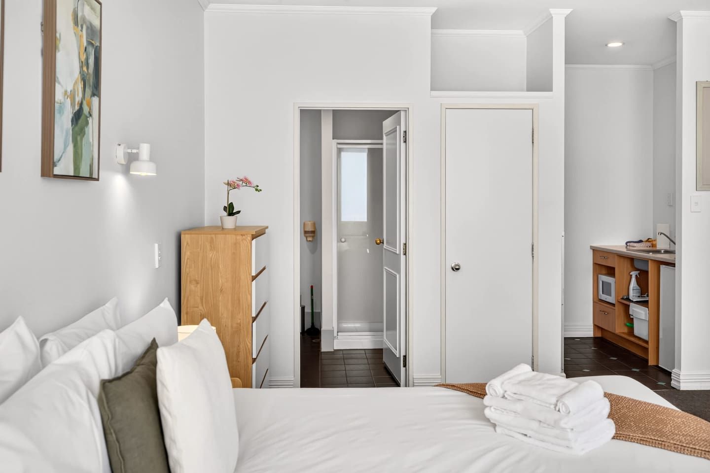 Ein Hotelzimmer mit Bett, einem Holzkoffer, einem Badezimmer mit Dusche und einer Küchenzeile.