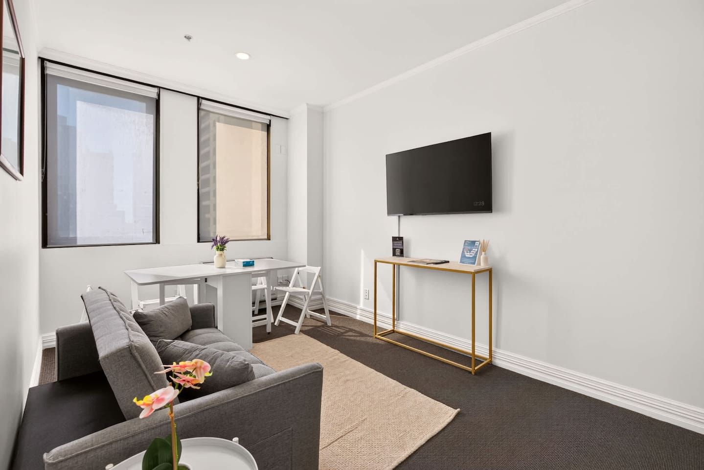 A modern living room with a grey sofa, a small table, and a TV mounted on the wall.