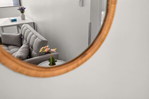 A room with a grey sofa, a small table with a vase of flowers, and a mirror reflecting the room's interior. - Stylish 1BR in the Heart of Auckland Zodiak Stays (Auckland)
