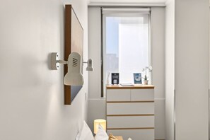 A hotel room with a bed, a bedside lamp, a wall-mounted light, a window with a view, and a small table with a plant and a sign. - Your Central Auckland City Escape Zodiak Stays (Auckland)