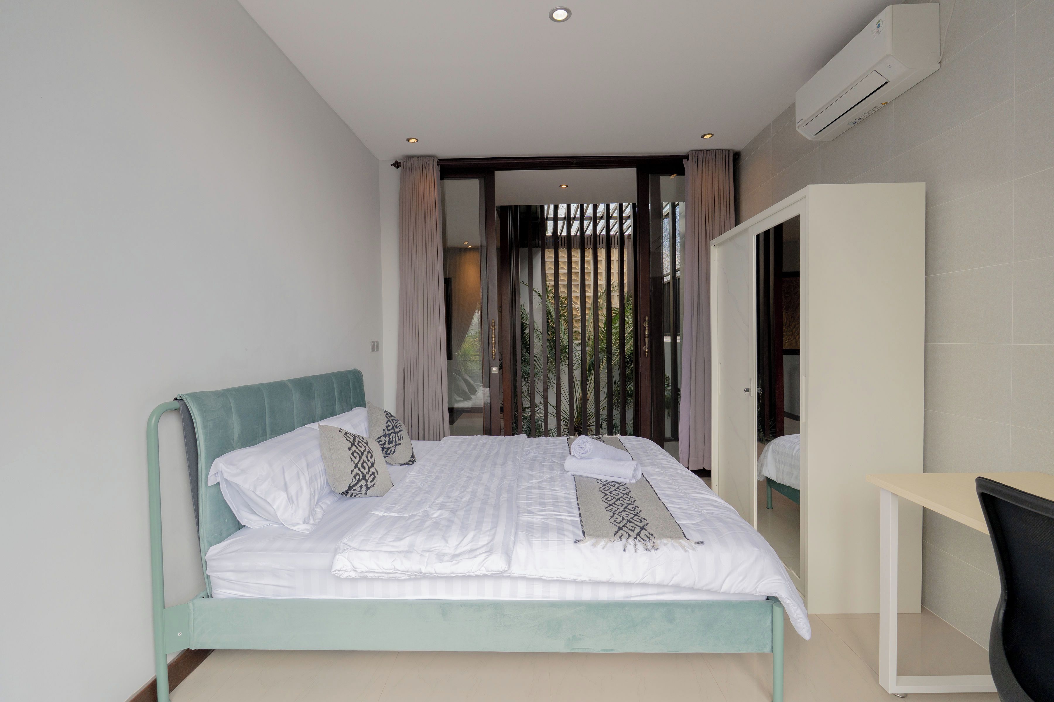 A modern bedroom with a bed, a desk, and an air conditioning unit.