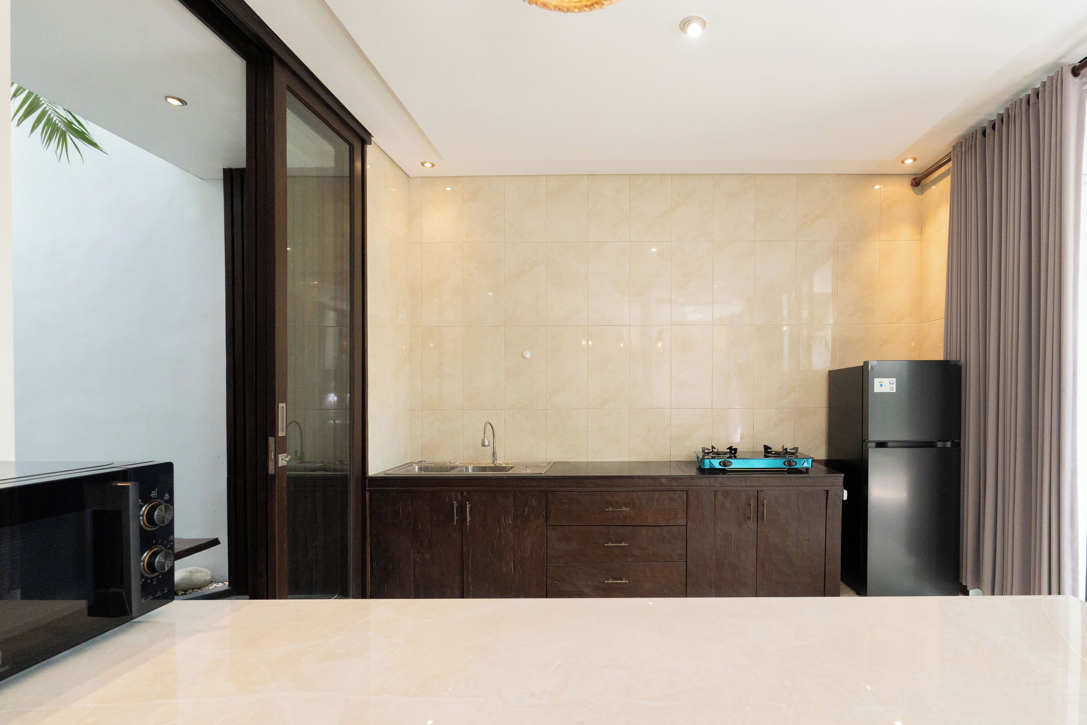 A modern kitchen with a dark wood cabinet, a stainless steel sink, and a black refrigerator.