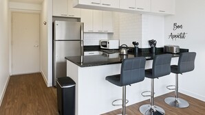 Una cocina moderna con armarios blancos, un refrigerador de acero inoxidable, una encimera negra y tres taburetes de bar.