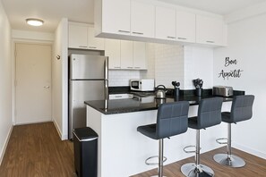 A modern kitchen with white cabinets, a stainless steel refrigerator, a black countertop, and three bar stools.