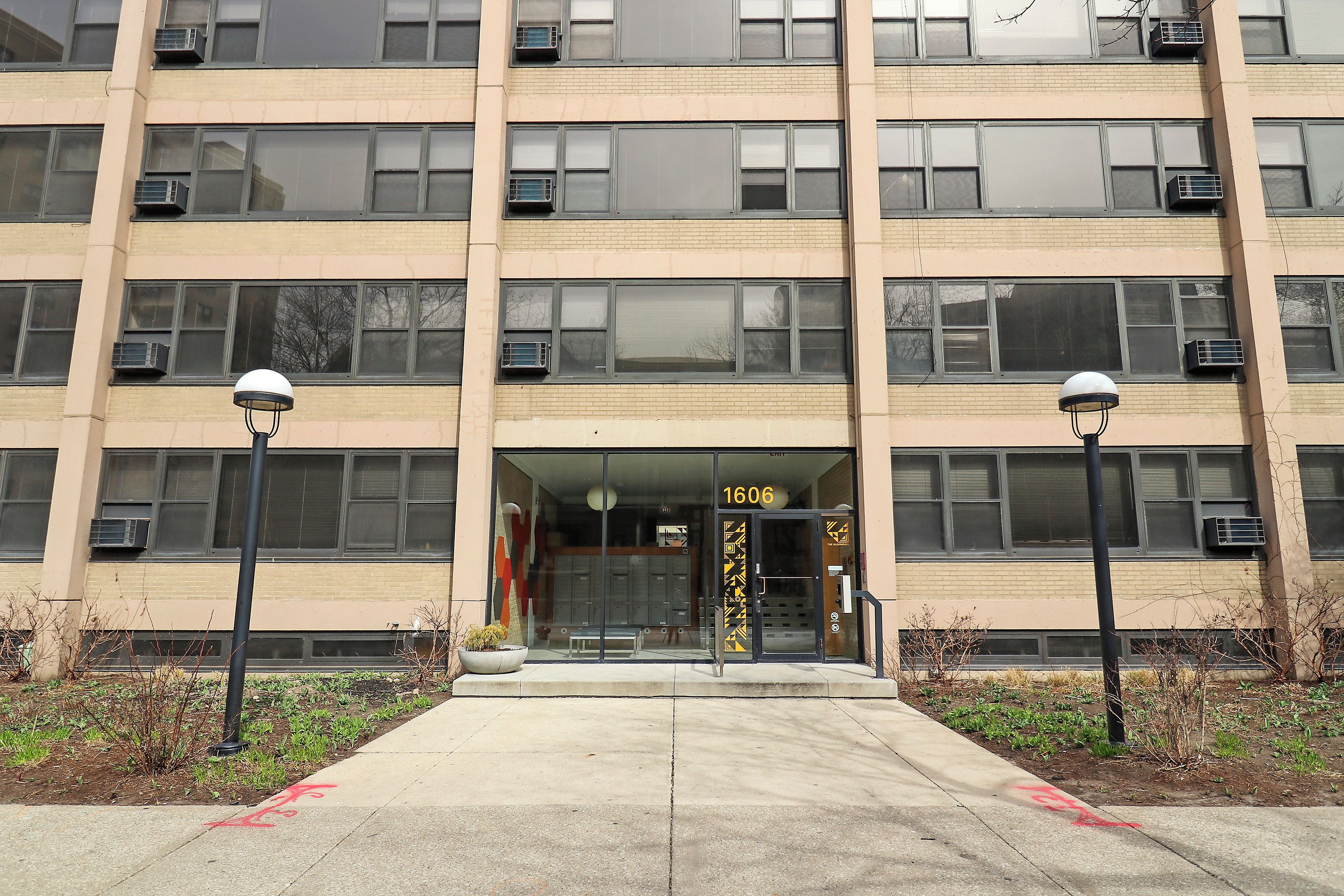Un edificio de varios pisos con fachada color beige, número 1606, que cuenta con entrada de vidrio y unidades de aire acondicionado.