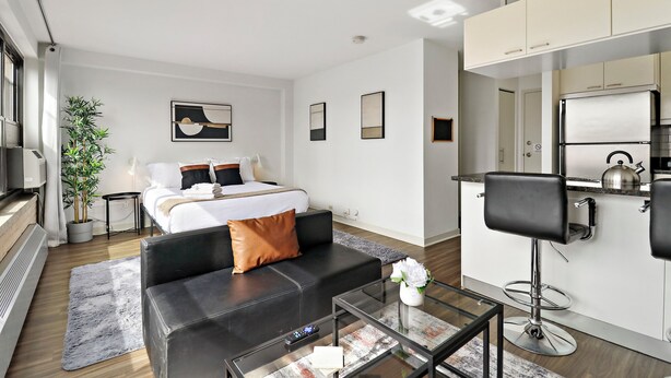 Una habitación de hotel moderna con cama, sofá, mesa de centro, televisor y kitchenette.