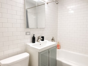 A bathroom with white tiled walls, a white sink with a faucet, a toilet, and a bathtub.