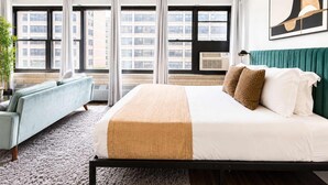 Una habitación de hotel con una cama, un sofá, un ventanal con cortinas y una planta.