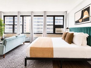Quarto de hotel com uma cama, um sofá, uma janela com cortinas e uma planta.