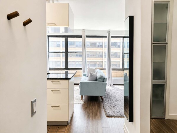 A modern apartment with a kitchen, a living area with a sofa, and large windows.