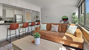 Un espace de vie moderne comprenant un ensemble de canapés, une table basse avec une plante et un coin cuisine avec des tabourets de bar.