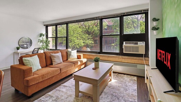 Un salon moderne avec une grande fenêtre, un canapé marron, une table basse et un téléviseur à écran plat.