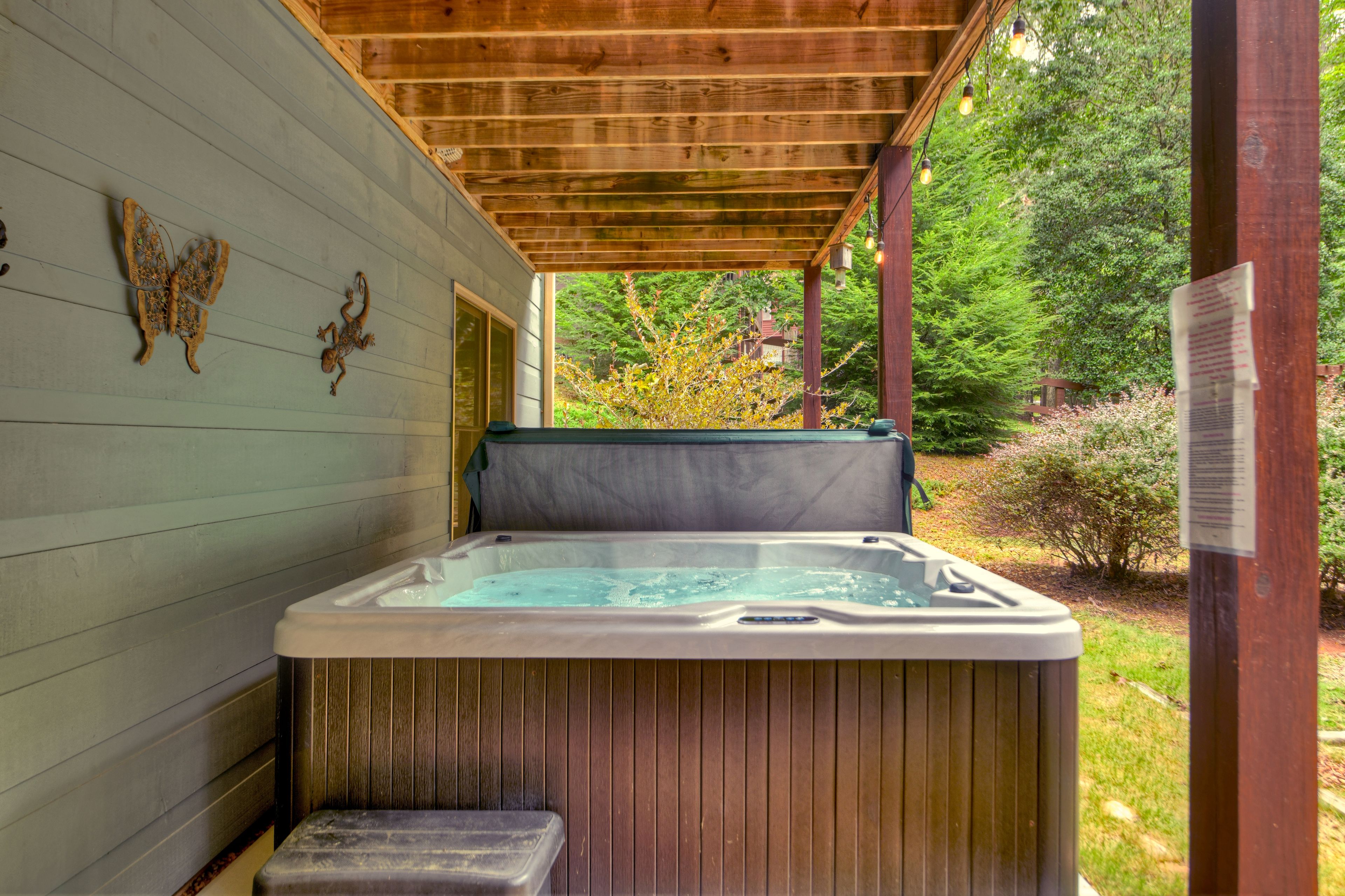 A hot tub under a wooden pergola with a view of a garden.