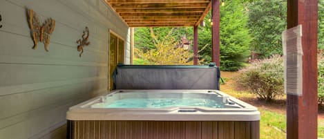 A hot tub under a wooden pergola with a view of a garden.