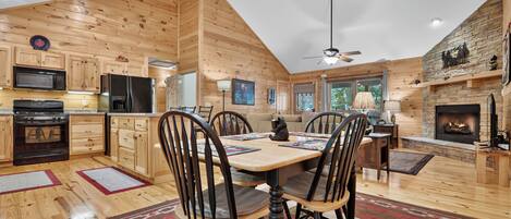Intérieur moderne d’une cabane en rondins, comprenant un coin repas, une cuisine et une cheminée.