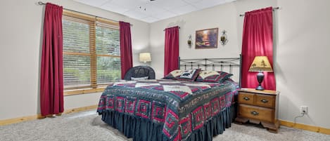 A bedroom with a bed, a nightstand, a lamp, a ceiling fan, and a window with curtains.