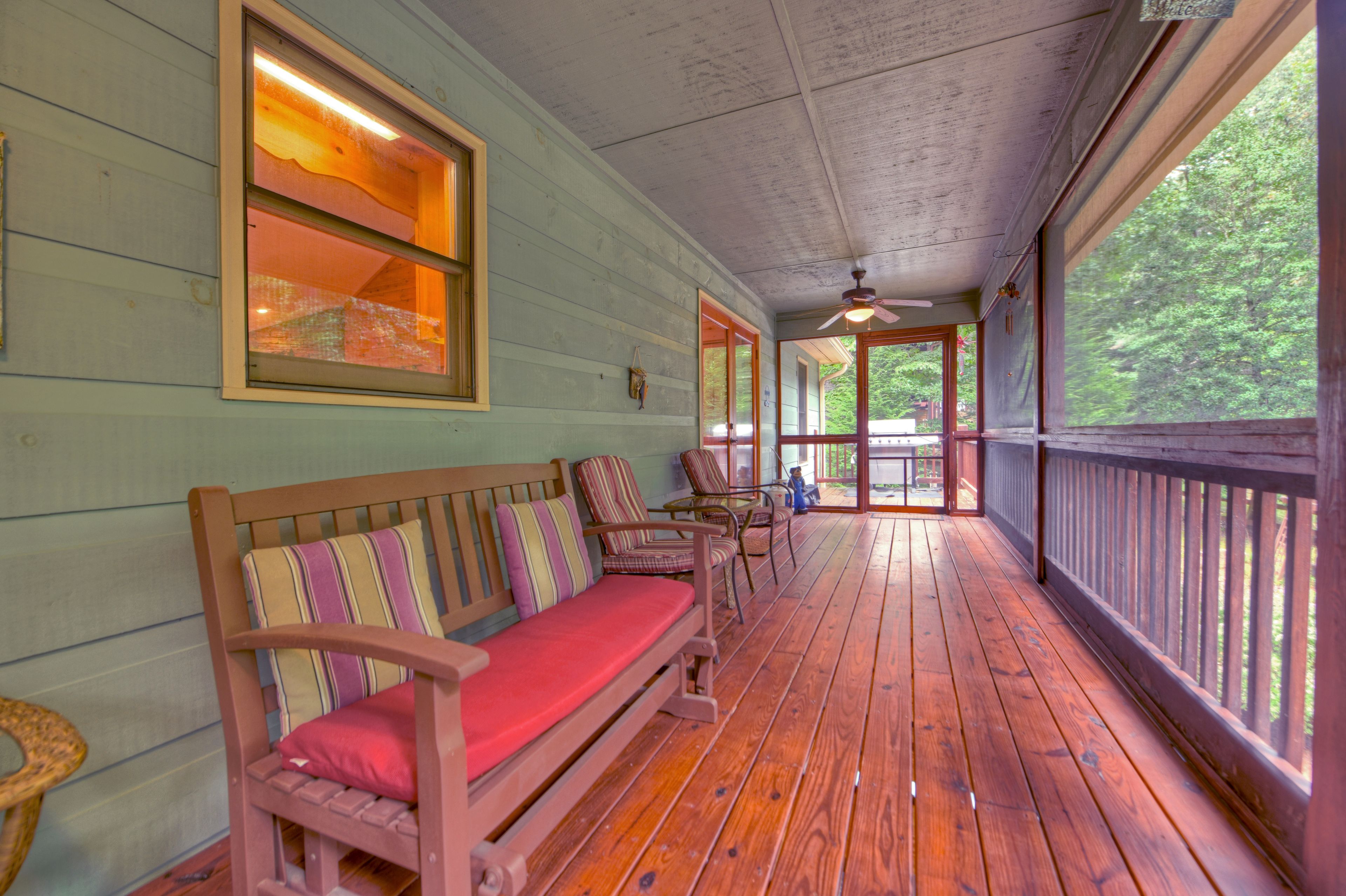 A covered porch with a wooden bench, chairs, and a ceiling fan.