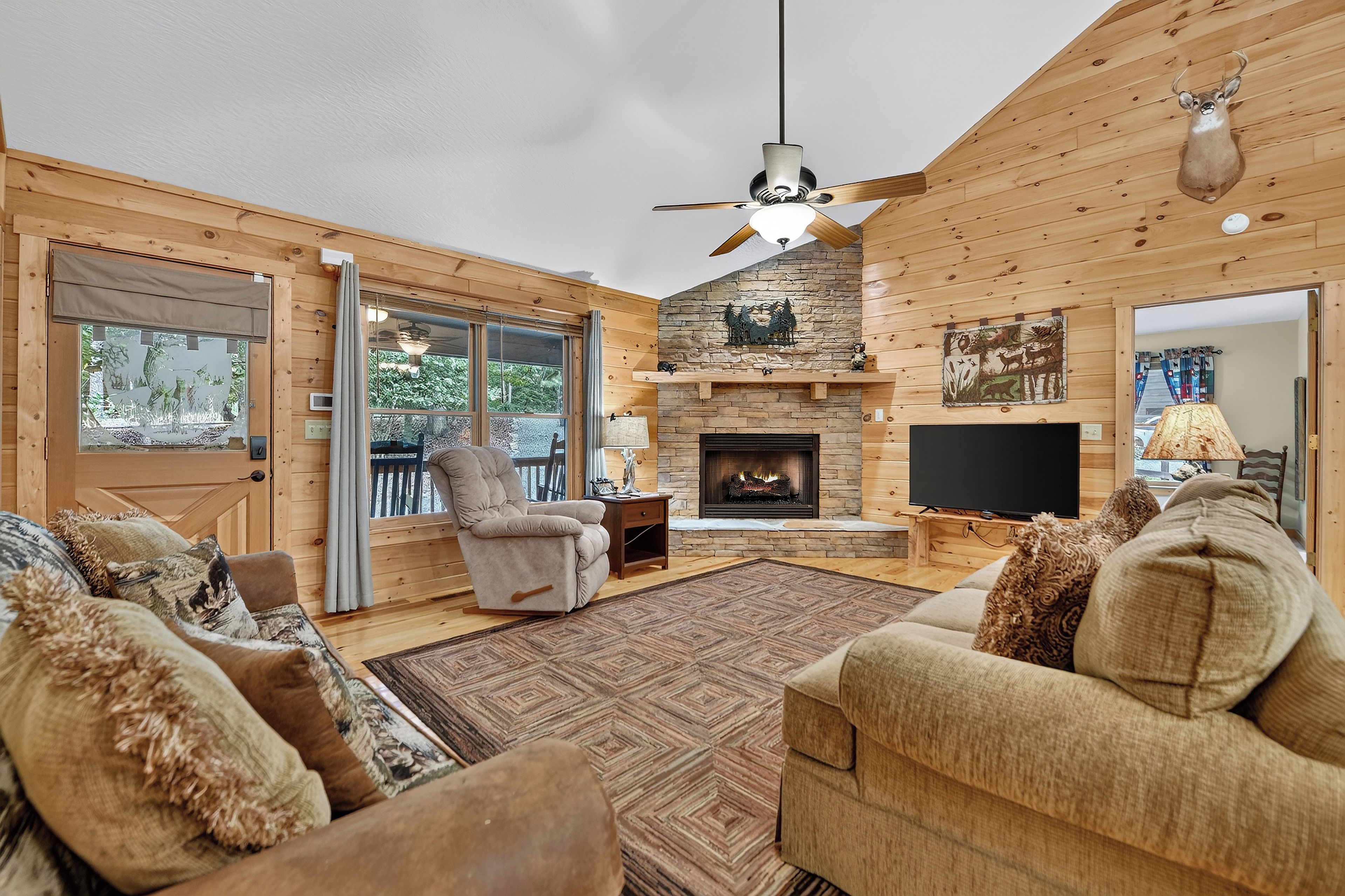 L’intérieur chaleureux d’un chalet en bois comprend une cheminée, des sièges confortables et une grande fenêtre donnant sur une terrasse.