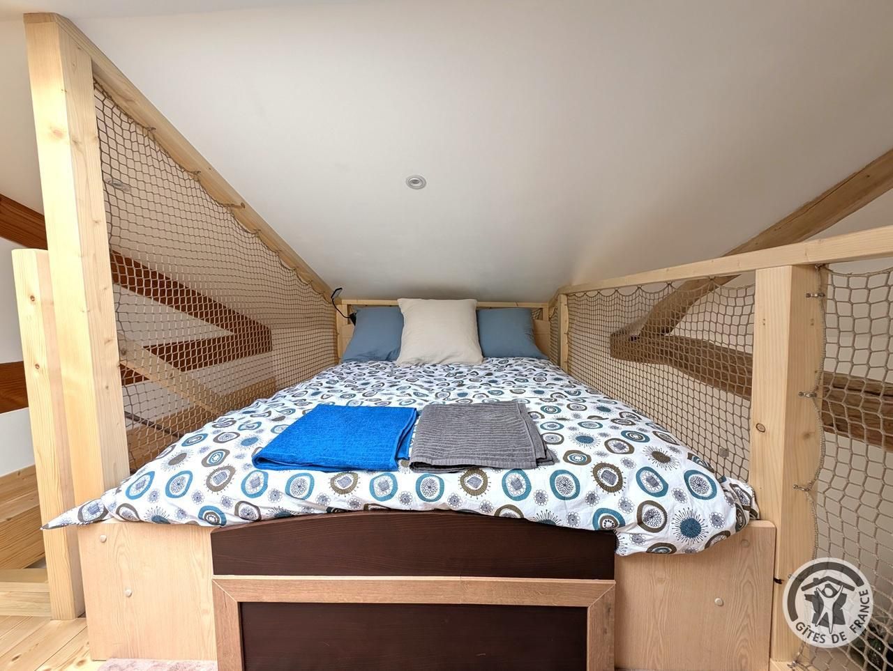 A single bed with a patterned bedspread, two pillows, and a folded towel.