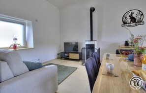 A modern living room with a sofa, a dining table with chairs, a TV, and a fireplace.