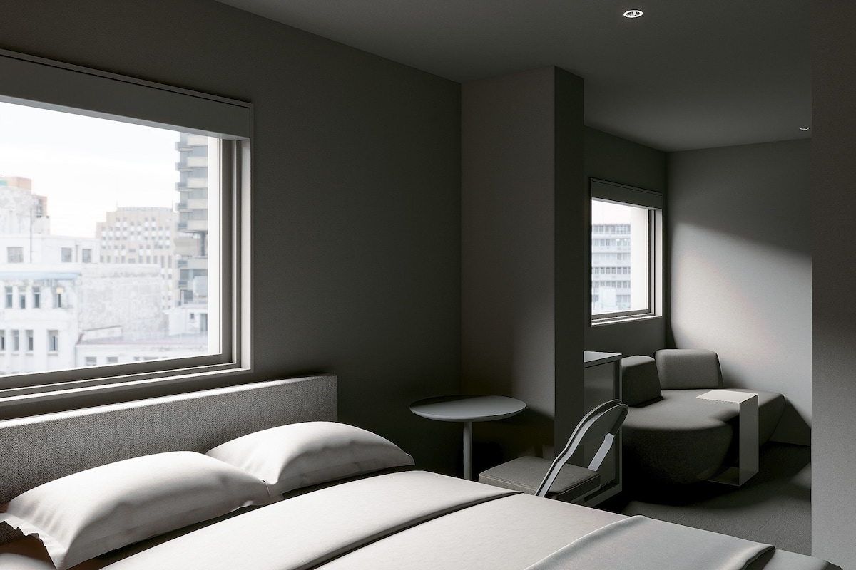 A modern hotel room with a large window, a bed with white linens, a small round table, and two chairs.