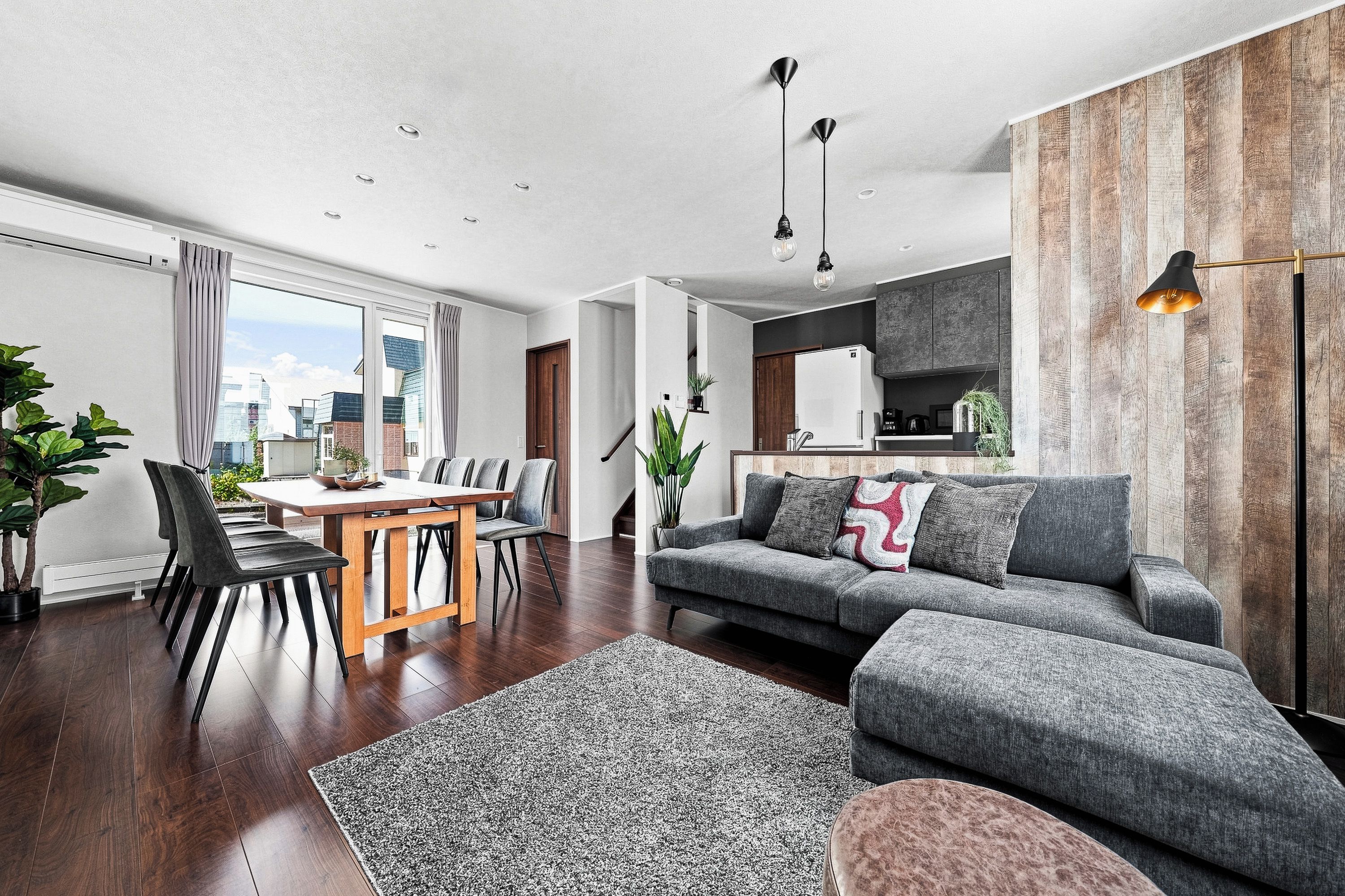 A modern living room with a dining area, a grey sofa, a coffee table, and a kitchen visible through an open doorway.
