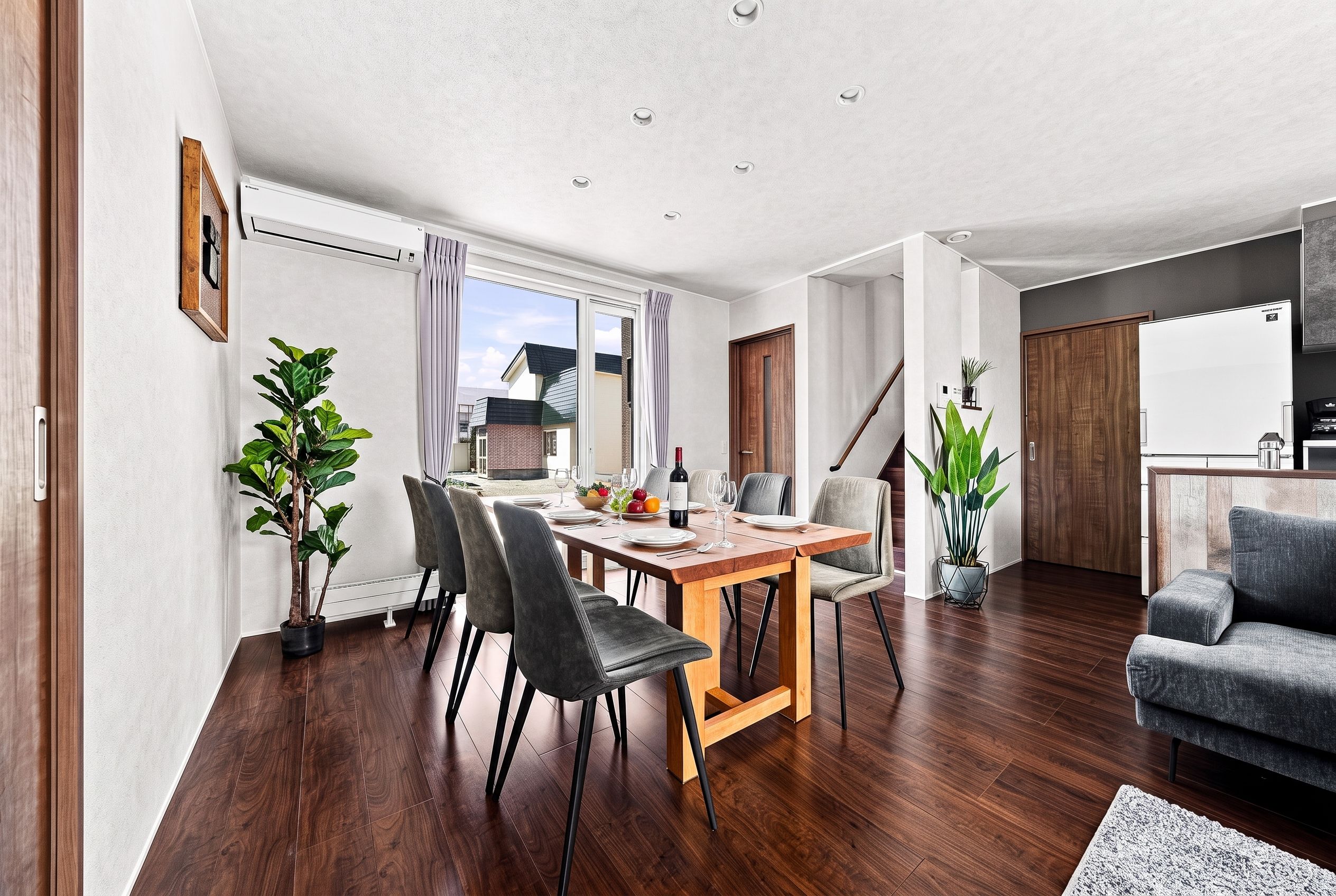 A modern living room with a dining area, wooden flooring, and a staircase leading to an upper level.