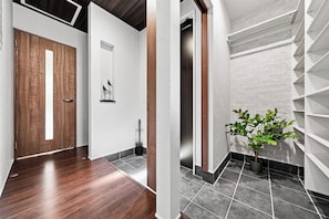 Un pasillo moderno con suelo de madera, una pared blanca con una obra enmarcada y una planta en maceta.