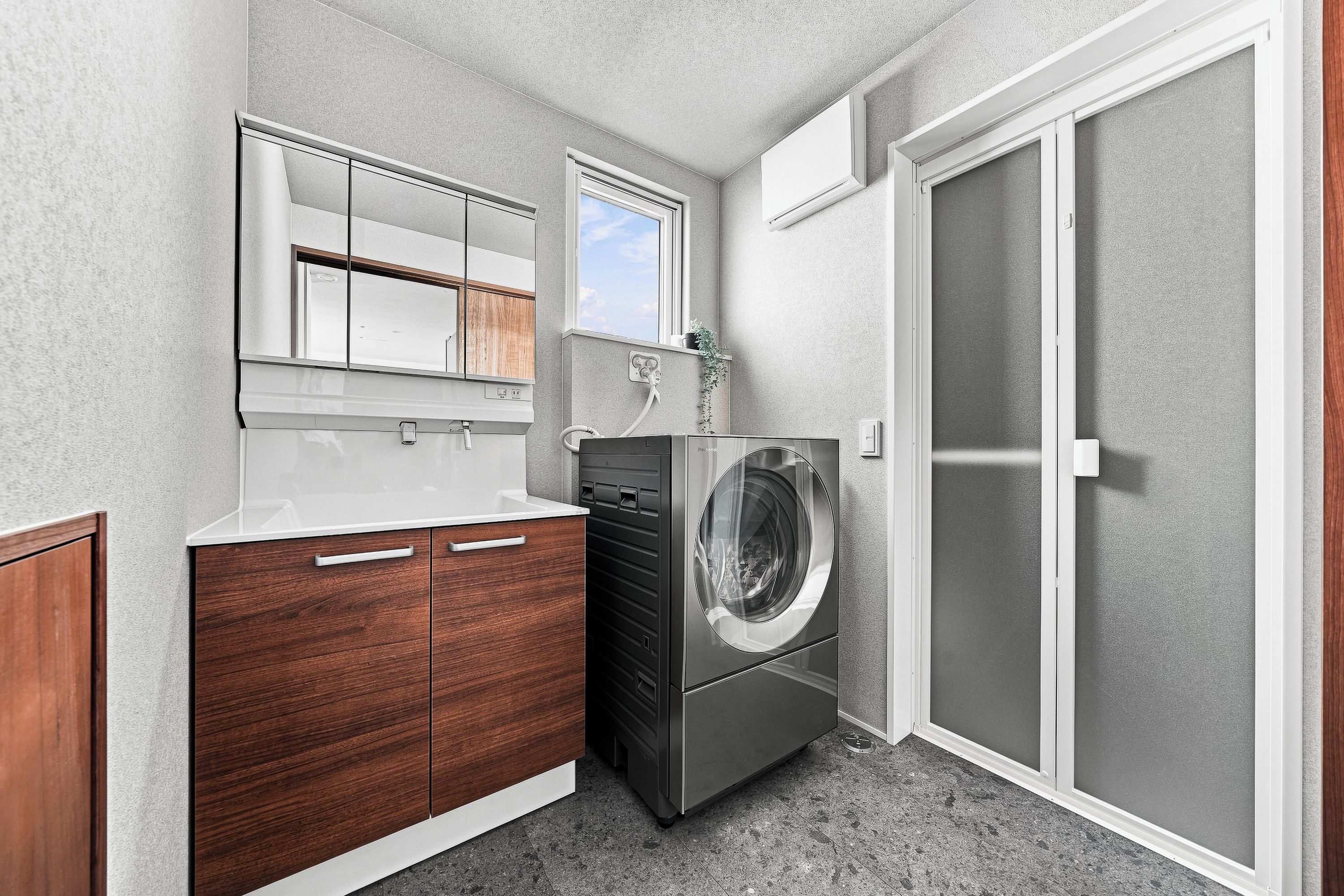 A compact laundry room with a built-in washer and dryer, wooden cabinetry, a mirror, and a sliding door closet.