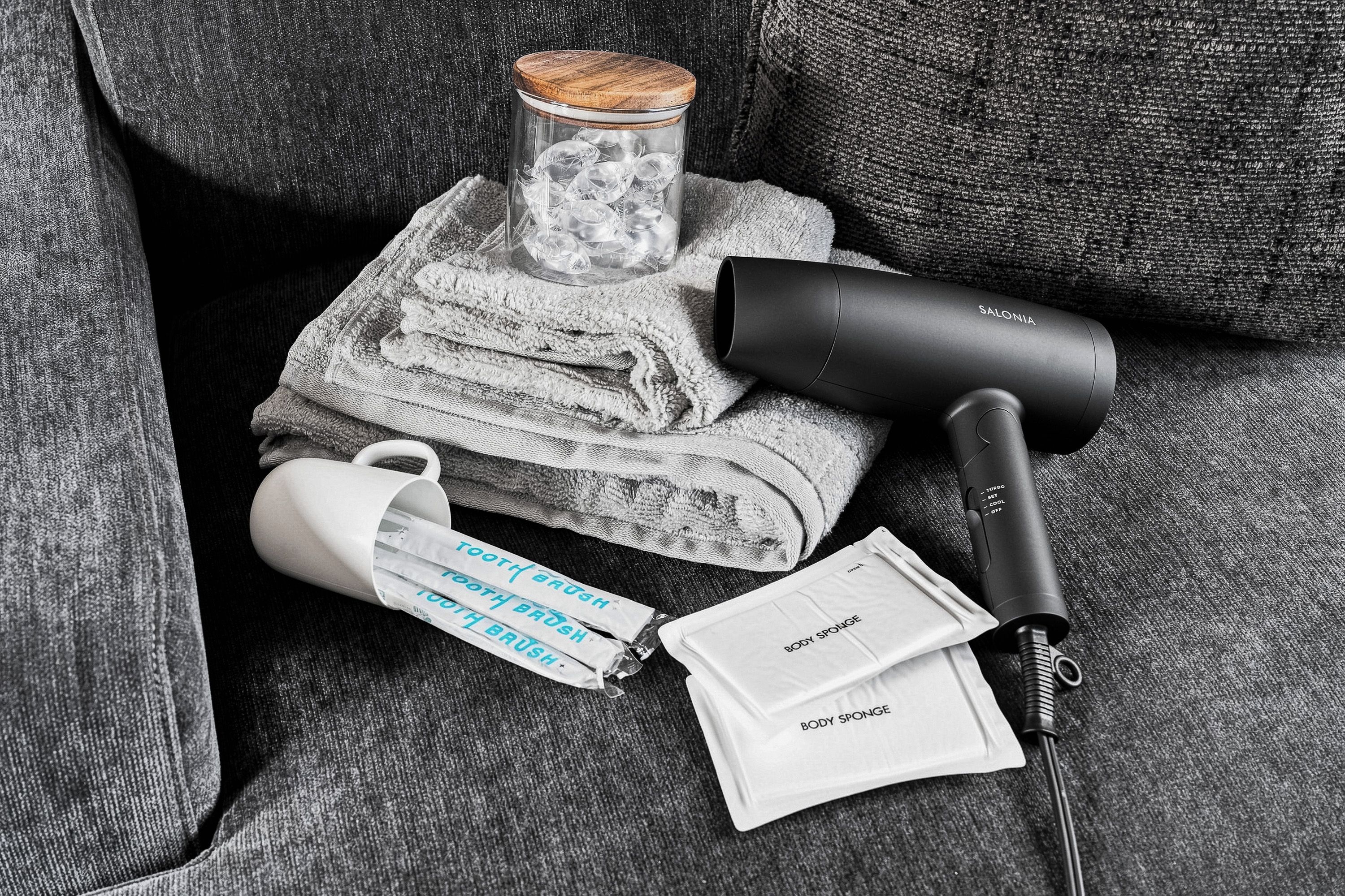 A hairdryer, a mug, and a body sponge on a grey couch.