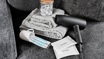 A hairdryer, a mug, and a body sponge on a grey couch.