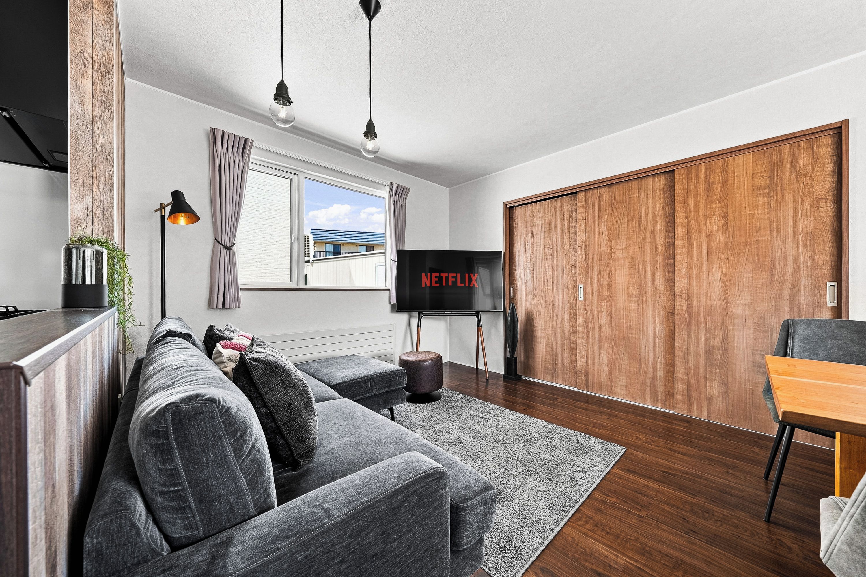 A modern living room with a grey sofa, wooden flooring, a TV, and a wardrobe.
