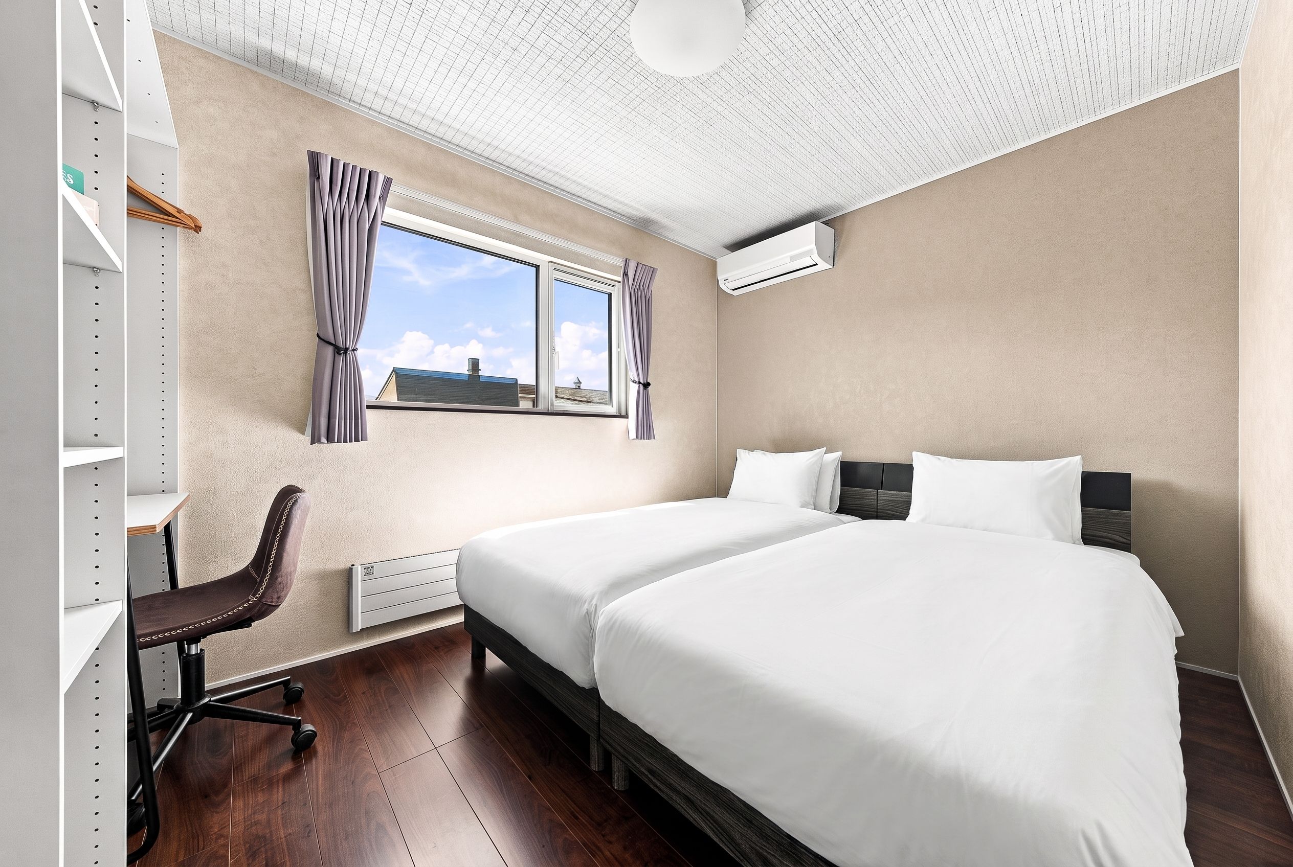 Habitación de hotel con dos camas, un escritorio, una silla, un radiador y un equipo de aire acondicionado.