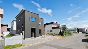 A modern residential building with a flat roof, large windows, and a gravel driveway.