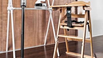 Une pièce avec un plancher en bois, un ventilateur sur pied, une chaise en bois et une structure tubulaire blanche adossée à un mur en bois.