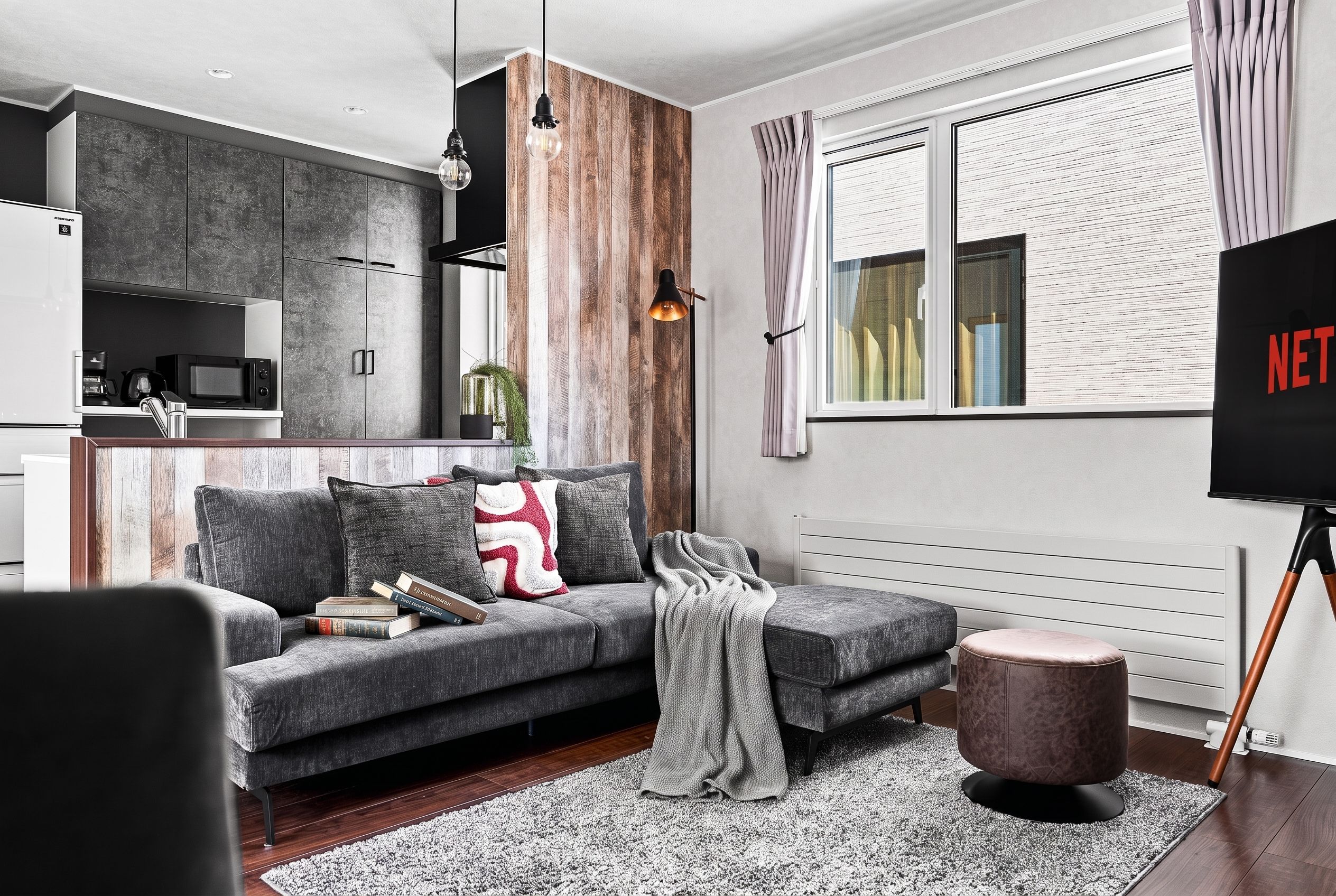 A modern living room with a grey sofa, a coffee table, a small round ottoman, and a TV mounted on the wall.
