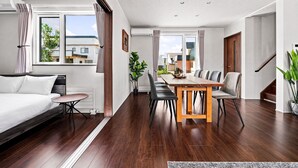 A modern living room with a sofa, a dining table with chairs, a staircase, and a view of the outside. - The Cross (Asahikawa)