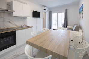 A modern kitchen with a built-in oven, a wooden countertop, and a dining area with a long table and white chairs. - Holiday flat with air conditioning (Bibione)