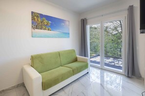 A room with a green sofa, a painting of a beach, and a large window with curtains. - Holiday flat with air conditioning (Bibione)