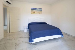 Ein Schlafzimmer mit einem Bett, einem weißen Nachtisch, einer weißen Toilette und einem Bild einer Strandlandschaft an der Wand.