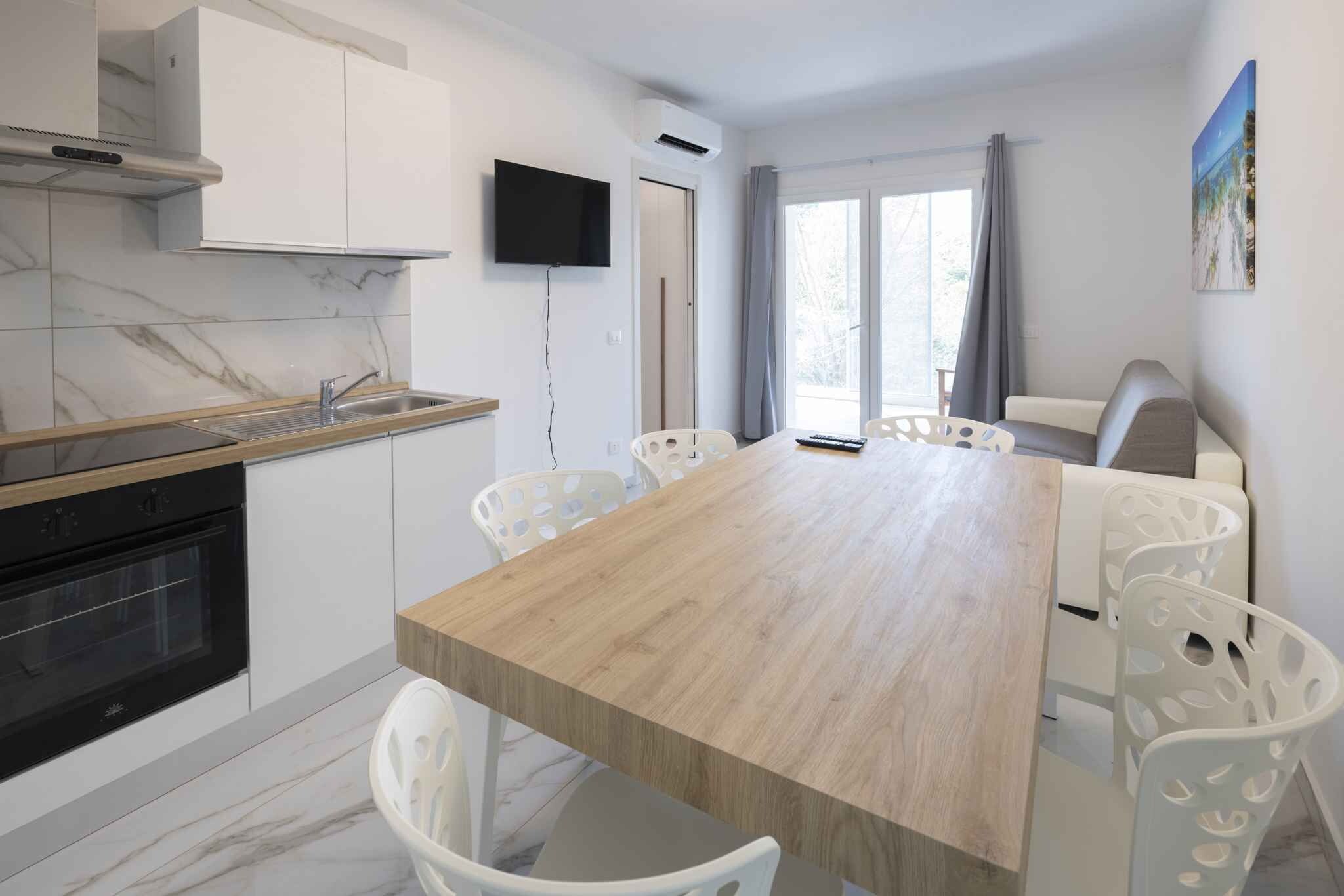 Una cocina moderna con horno empotrado, encimera de madera y lavabo. Cuenta con un comedor con mesa de madera y sillas blancas.