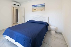 A bedroom with a bed, a painting of a beach scene, a white toilet, and an air conditioning unit. - Holiday apartment with air conditioning (Bibione)