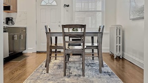 Un coin repas avec une table et des chaises en bois, une porte blanche et une fenêtre avec des stores.