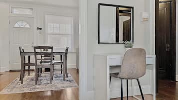 Un coin repas avec une table et des chaises, un bureau blanc avec une chaise, un miroir et un radiateur.
