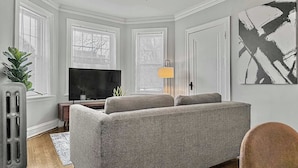 Un salon avec un canapé gris, un téléviseur, un ventilateur de plafond et un radiateur.