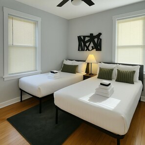 A hotel room with two beds, a ceiling fan, and a wall-mounted abstract art piece. - 1BR Unit w/ 2 Comfy Beds (Chicago)