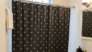 A bathroom with a black and white polka dot shower curtain, a white sink with a black faucet, and a white toilet. - Hyde Park Trendy Studio Apartment in Good Spot (Chicago)